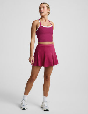 Woman wearing a red cropped tank top and magenta mini skirt against a plain background. 