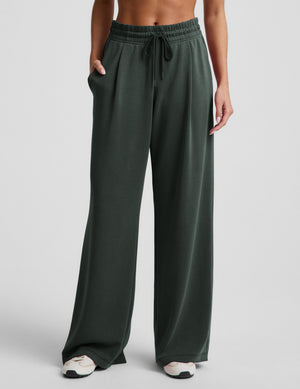 Woman wearing a white bra and green wide leg pants against a plain background. 