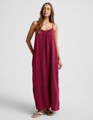 Woman wearing a red maxi cupro dress against a plain background. 