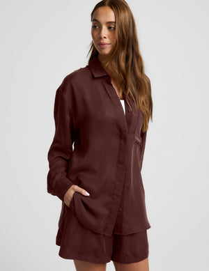 Woman wearing a brown button up shirt and shorts against a plain background. 