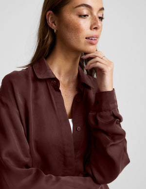 Woman wearing a brown button up shirt and shorts against a plain background. 