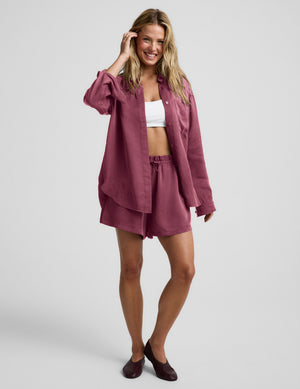 Woman wearing a purple button down shirt and shorts against a plain background. 