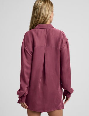 Woman wearing a purple button down shirt and shorts against a plain background. 