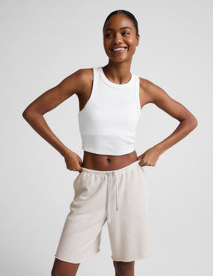 Woman wearing Beige Fade Out Low-Rise Bermuda Short™ paired with a white tank top, featuring drawstrings and a raw hem.