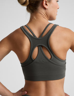 Woman wearing a green sports bra and shorts against a plain background. 