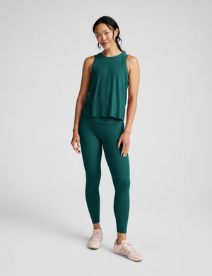 Woman wearing a green tank top and leggings against a light gray background. 