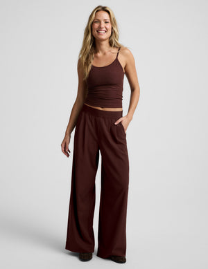 Woman wearing a brown waist length tank top and brown trousers against a plain background. 