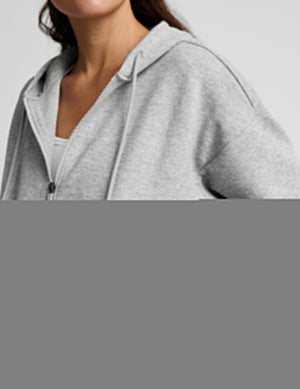 Woman wearing a gray zip-up sweatshirt and gray wide leg pants against a plain background. 