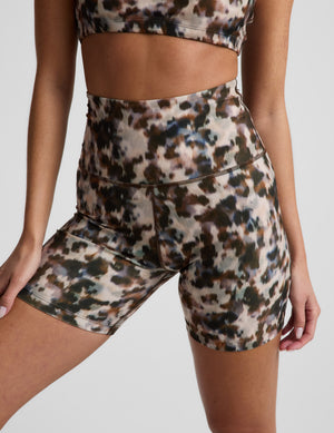 Woman in a printed sports bra and biker shorts against a plain background. 