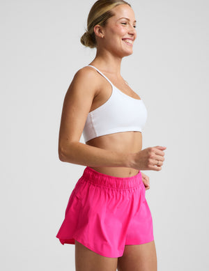 Woman wearing a white sports bra and pink running shorts against a plain background. 