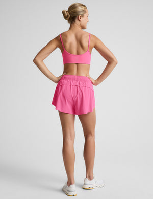 Woman wearing a pink sports bra and pink running shorts against a plain background. 