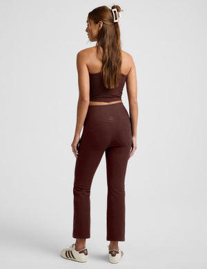 Woman wearing a brown cropped tank top and brown kick flare pants cropped pants against a plain background. 