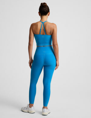 Woman wearing a blue cropped tank top and blue high-waisted midi leggings against a plain background. 