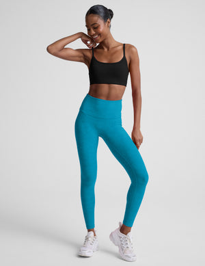 Woman wearing a black sports bra and blue leggings on a white background. 