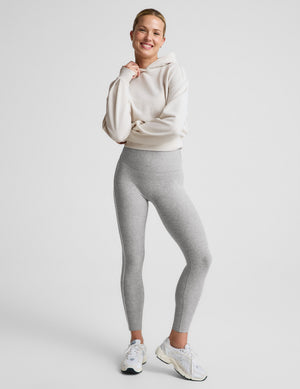 Woman wearing a gray sports bra and leggings with white contrast piping on a plain background. 