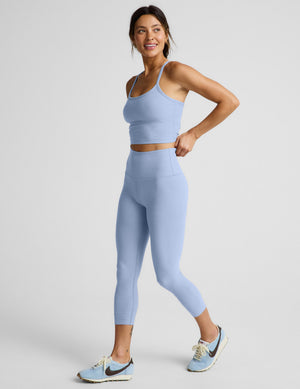 Woman wearing a blue cropped racerback tank and leggings against a plain background. 