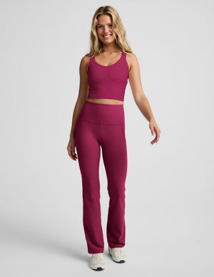 Woman wearing a red cropped tank with a twist cutout back detail and red pants against a plain background. 