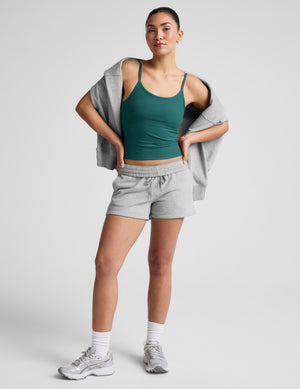 Woman wearing a green tank top and gray sweat shorts on a light gray background. 