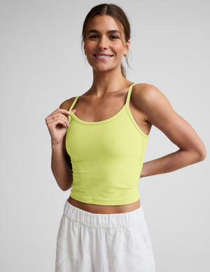Woman wearing a yellow waist length tank and white linen pants against a plain background. 