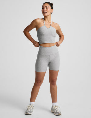 Woman wearing a gray strappy cropped tank and biker shorts against a plain background. 