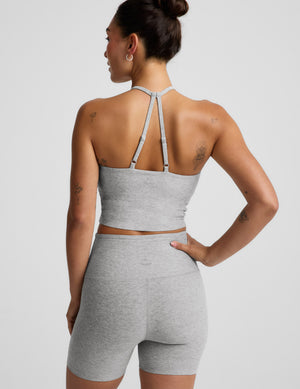 Woman wearing a gray strappy cropped tank and biker shorts against a plain background. 