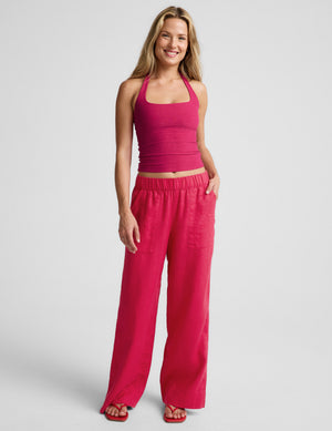 Woman wearing a red halter top and red linen pants against a plain background. 