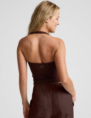 Woman wearing a brown halter tank top and brown linen pants against a plain background. 