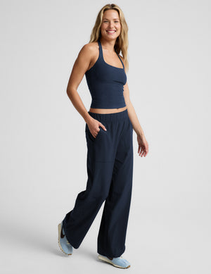 Woman wearing a navy blue halter tank and blue pants against a plain background. 