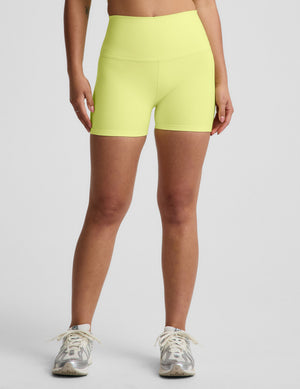 Woman wearing a yellow cropped tank top and biker shorts against a plain background. 