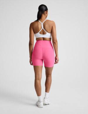 Person wearing a white sports bra and pink high-waisted shorts on a plain background. 