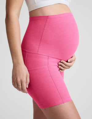 Woman wearing a white bra and pink maternity shorts against a plain background. 