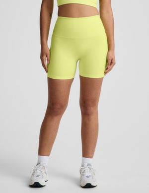 Woman wearing a bright yellow cropped tank top and biker shorts against a plain background. 