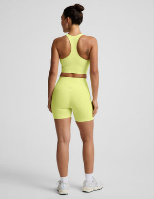 Woman wearing a bright yellow cropped tank top and biker shorts against a plain background. 