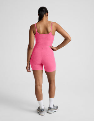 Woman wearing a pink sleeveless biker jumpsuit against a plain background. 