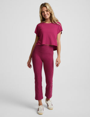 Woman wearing a magenta cropped short sleeve and magenta pintuck capri pants against a plain background. 