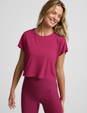 Woman wearing a magenta cropped short sleeve and magenta pintuck capri pants against a plain background. 