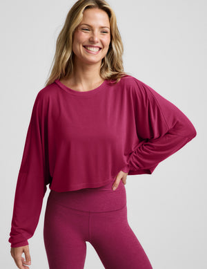 Woman wearing a cropped magenta long sleeve top and high-waisted midi length leggings against a plain background. 