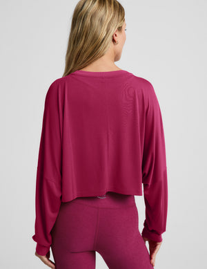 Woman wearing a cropped magenta long sleeve top and high-waisted midi length leggings against a plain background. 