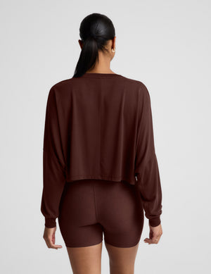 Woman wearing a brown long sleeve cropped top and brown biker shorts against a plain background. 