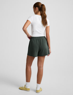 Woman wearing a white t-shirt and green skort against a plain background. 