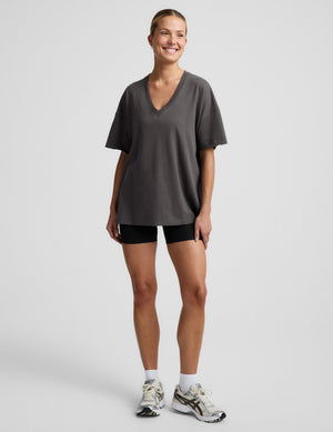 Woman wearing a black v-neck shirt and black biker shorts against a plain background. 
