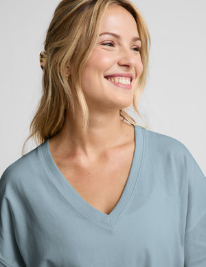 Woman wearing a blue v-neck oversized t-shirt and blue shorts against a plain background. 