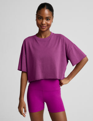 Woman wearing a purple cropped t-shirt and purple biker shorts against a plain background. 