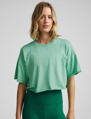 Woman wearing a light green cropped t-shirt and green biker shorts against a plain background. 