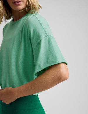 Woman wearing a light green cropped t-shirt and green biker shorts against a plain background. 