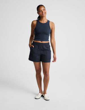 Woman wearing a navy ribbed tank top and linen shorts against a plain background. 