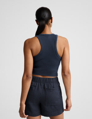 Woman wearing a navy ribbed tank top and linen shorts against a plain background. 