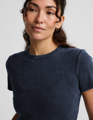 Woman wearing a navy blue ribbed t-shirt and white linen shorts against a plain background. 