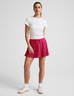 Woman wearing a white ribbed t-shirt and red skirt against a plain background. 