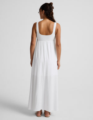Woman wearing a white sleeveless dress on a plain background. 